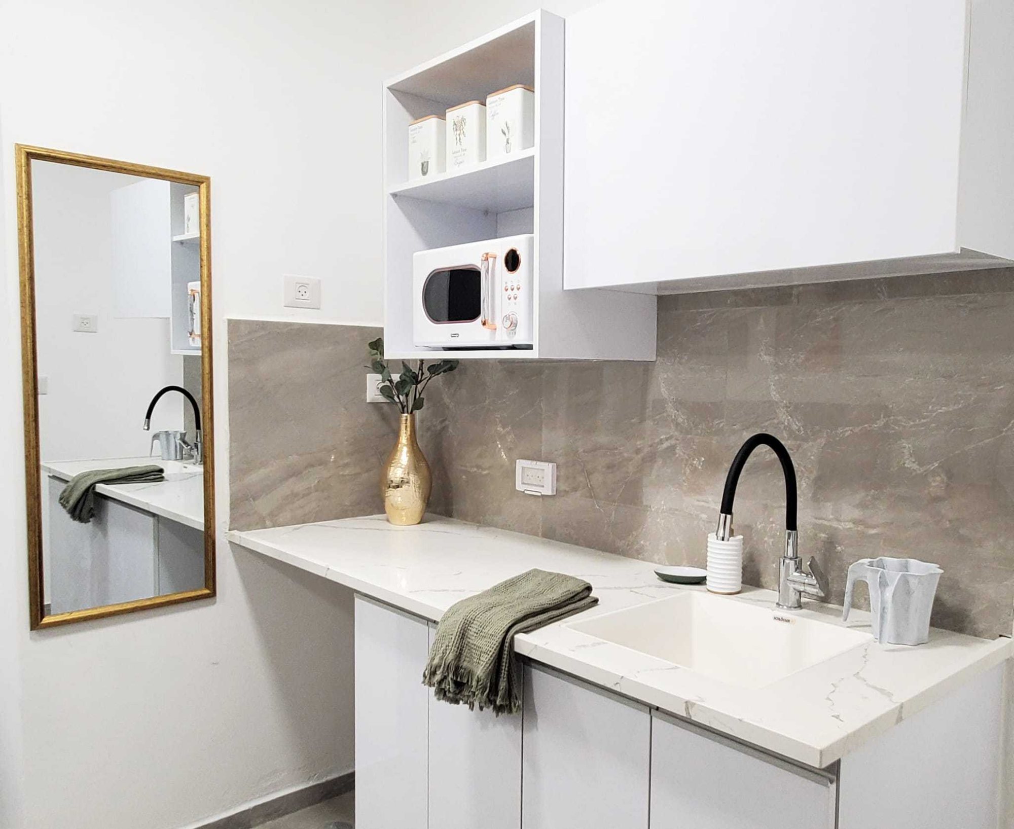 Kitchenette with sink, microwave, storage and a gold-framed mirror